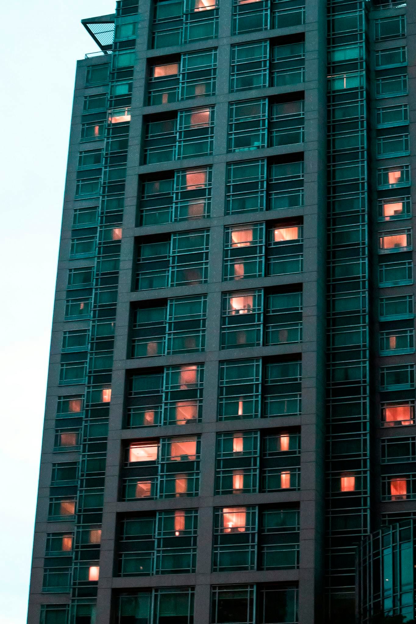 Photograph of a modern skyscraper with glowing windows at dusk, showcasing urban architecture.